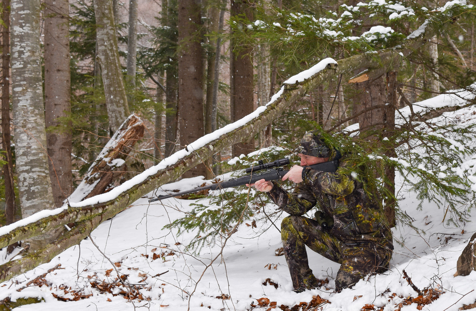 Person in snow wearing pinyon pine camouflage using a spotting scope.